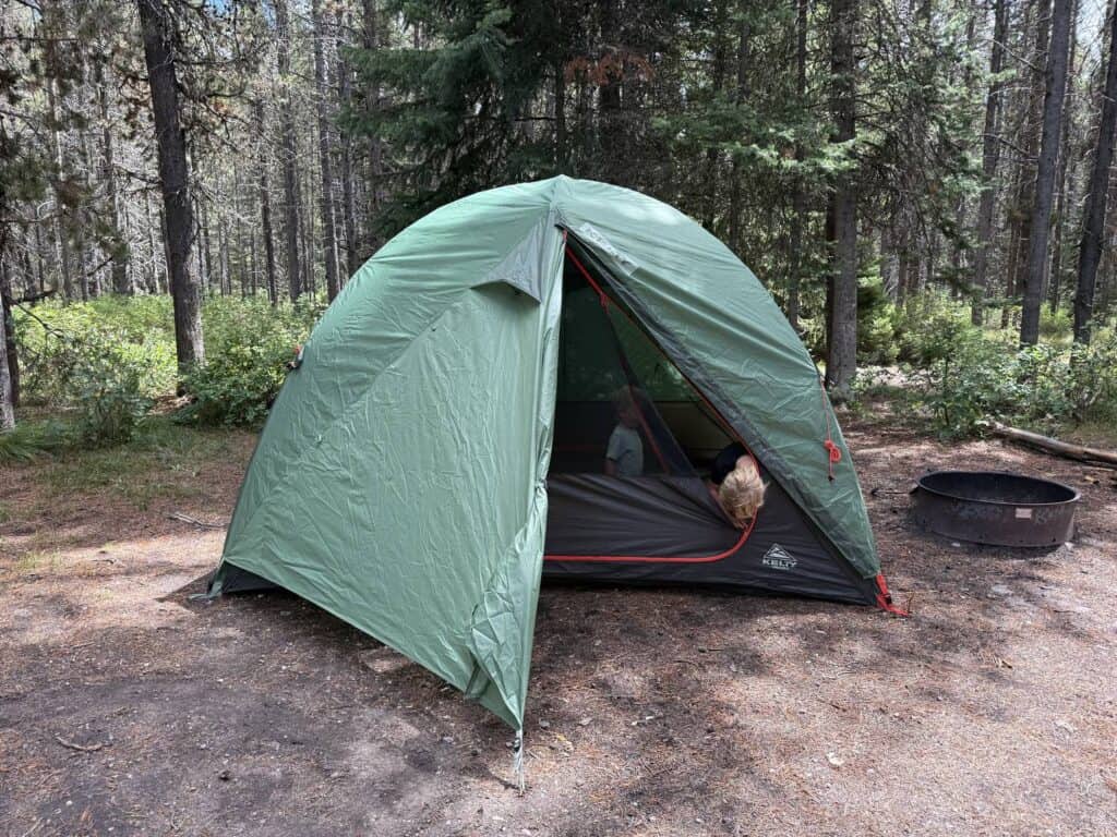 Kelty Wireless 6 with the rainfly door rolled back and a child sitting inside the tent