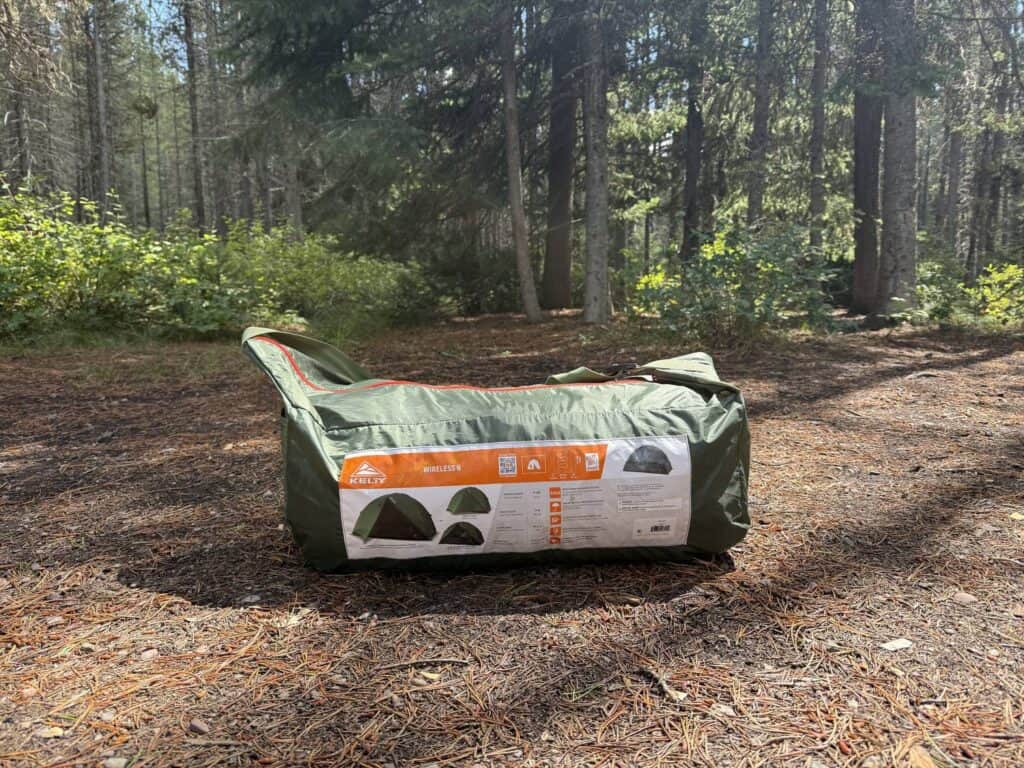 Kelty Wireless 6 packed in its green duffel carry bag on the ground at a forest campsite
