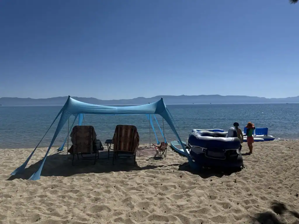 A blue Rhino Valley shade canopy shelters two low beach chairs and an inflatable float on a Lake Tahoe beach.