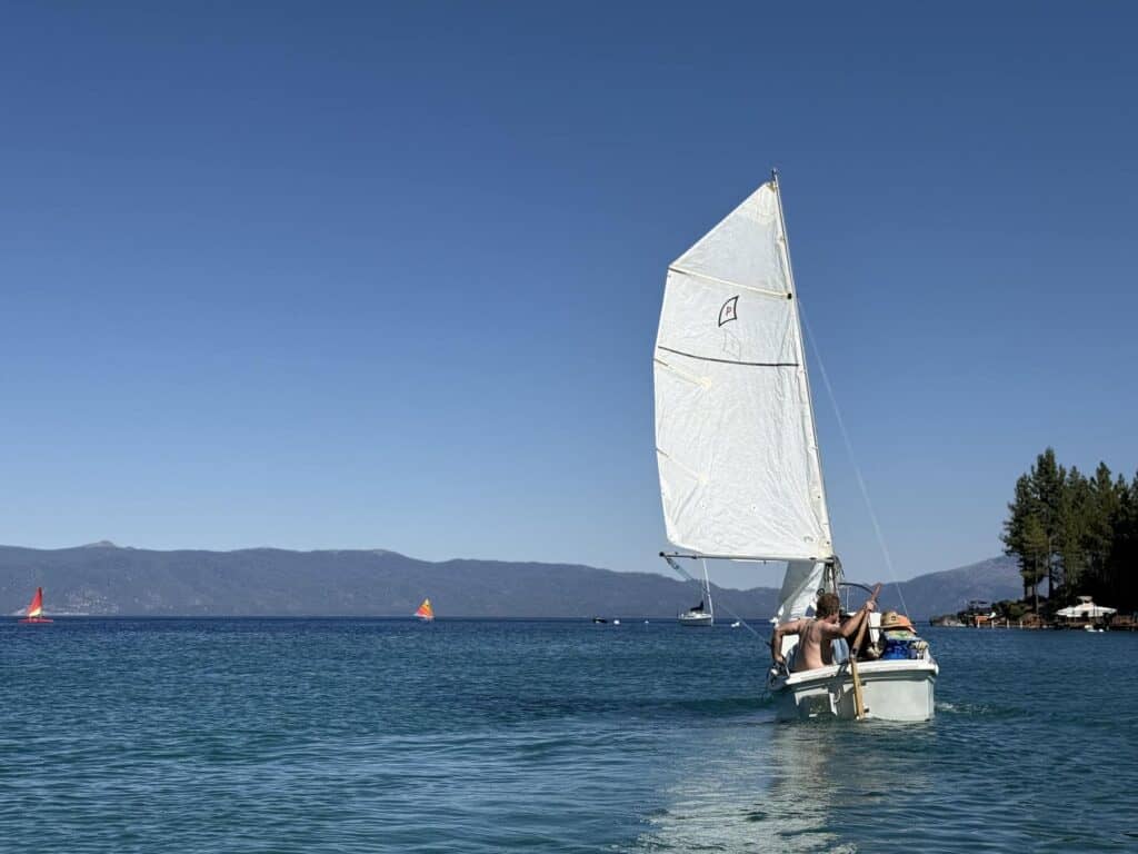 A white sailboat cruises across deep blue Lake Tahoe with mountains on the far shore.