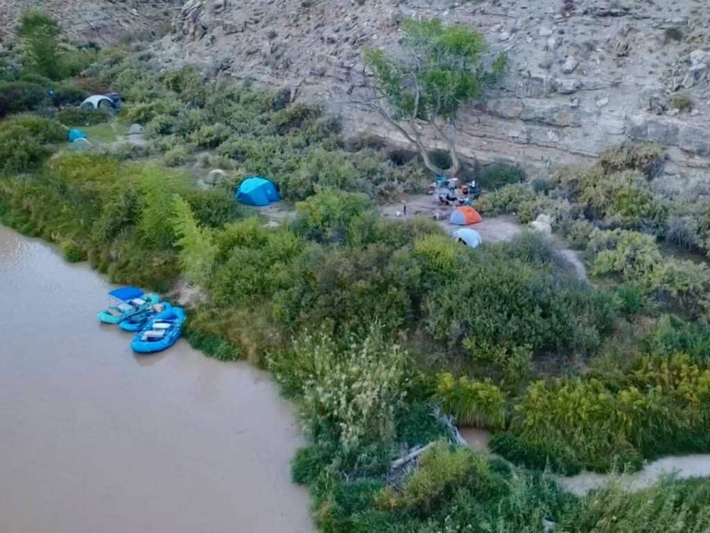 Aerial view of a riverside camp with rafts tied at the bank and the orange Marmot Tungsten among other tents in the brush