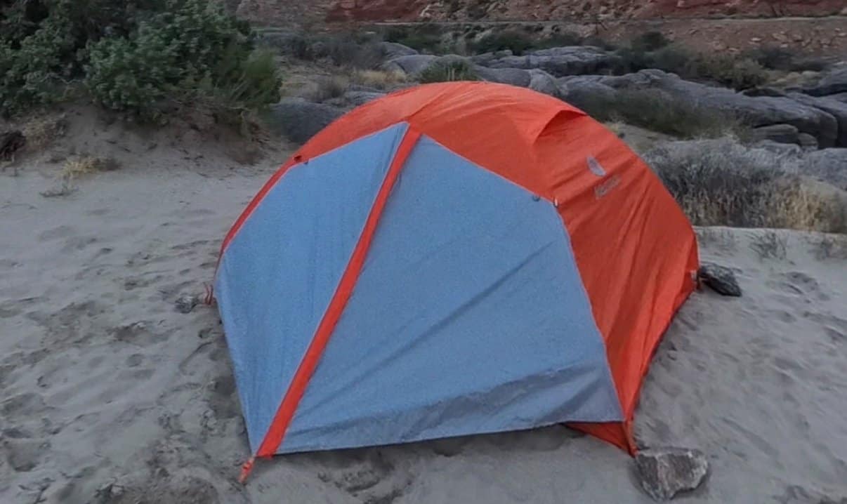 Marmot Tungsten tent with an orange and grey rainfly pitched on sand below red canyon walls