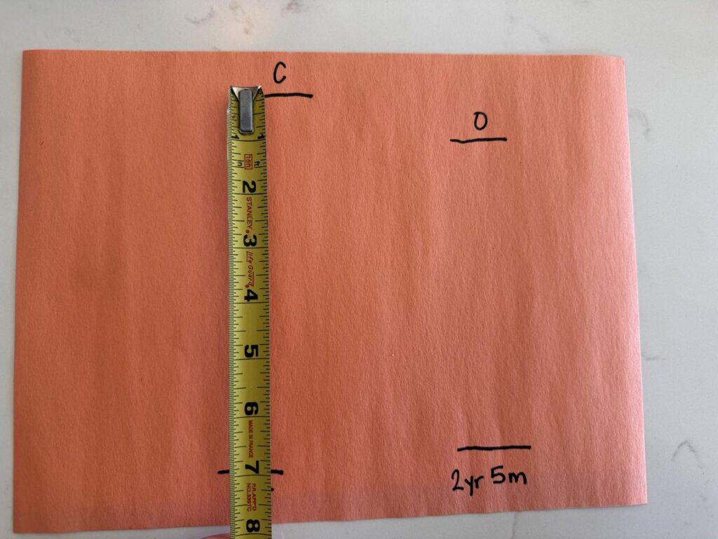 Tape measure laid across orange paper from a toe line to a heel line to measure a child's foot length