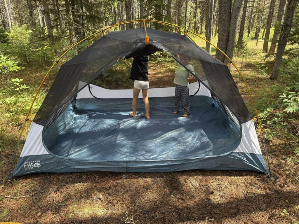 Two children standing inside the mesh tent body of the Mountain Hardwear Mineral King 3 in a forest