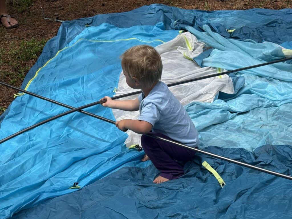 Toddler holding a tent pole on top of the laid-out NEMO Aurora Highrise 6 before setup