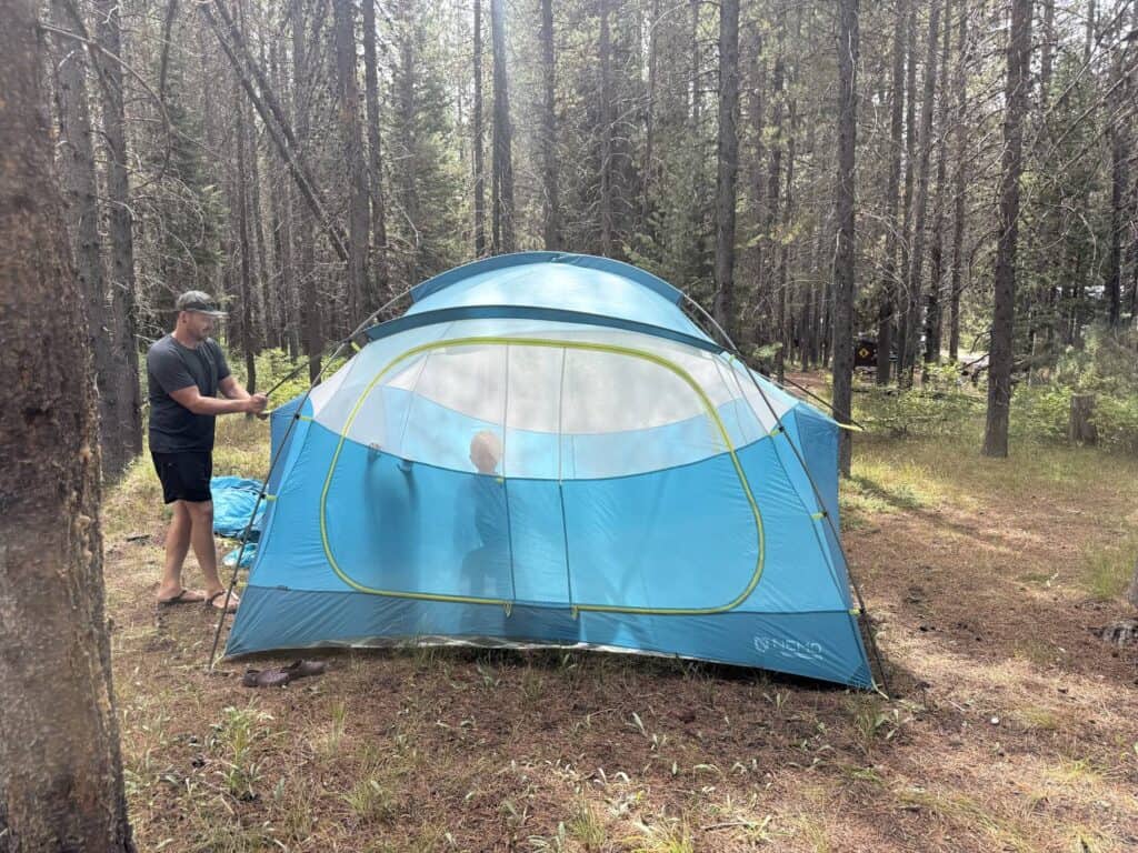 Adult pitching the NEMO Aurora Highrise 6 tent body in a pine forest