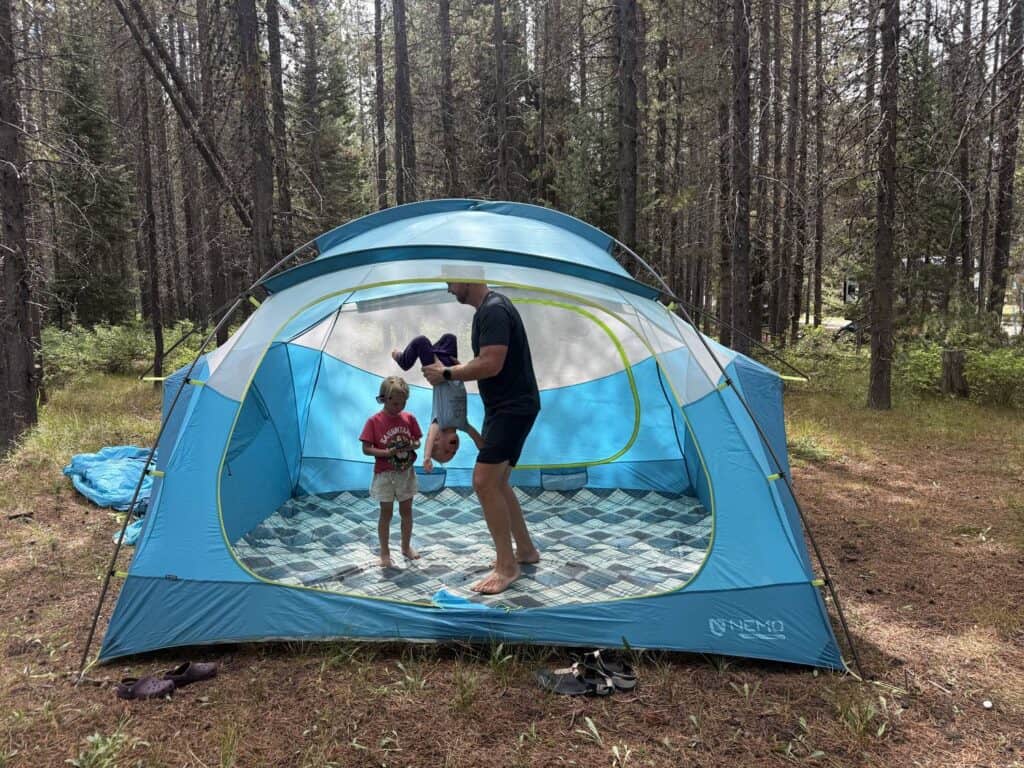 Adult holding a child upside down inside the NEMO Aurora Highrise 6 tent body while another child stands nearby