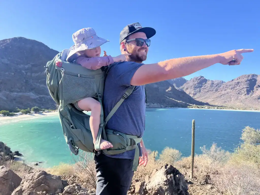 Dad pointing out a turquoise lake with a toddler riding in the Osprey Poco Premium child carrier
