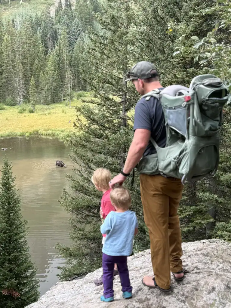 Dad and two kids on a rock overlooking a mountain lake, wearing the Osprey Poco Premium child carrier