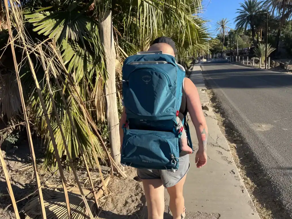 Adult walking along a road in San Ignacio carrying the Osprey Poco SLT child carrier