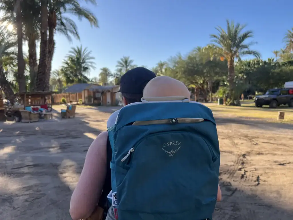 Adult carrying a baby in the Osprey Poco SLT child carrier on a sandy road in San Ignacio