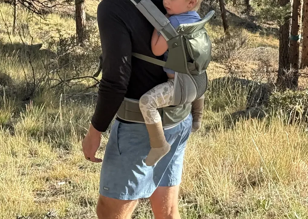 Dad hiking through pine forest with a toddler on his back in the Osprey Poco Soft child carrier