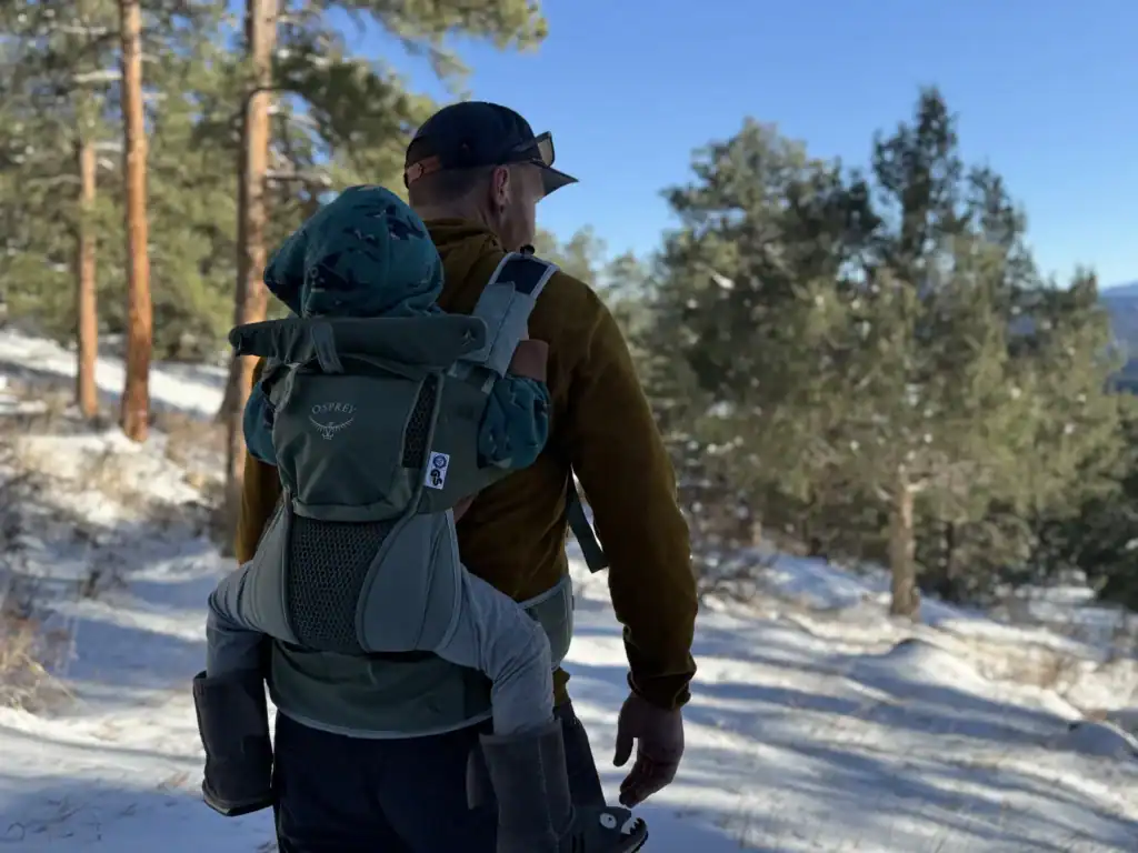 Dad on a snowy trail carrying a baby in the Osprey Poco Soft child carrier