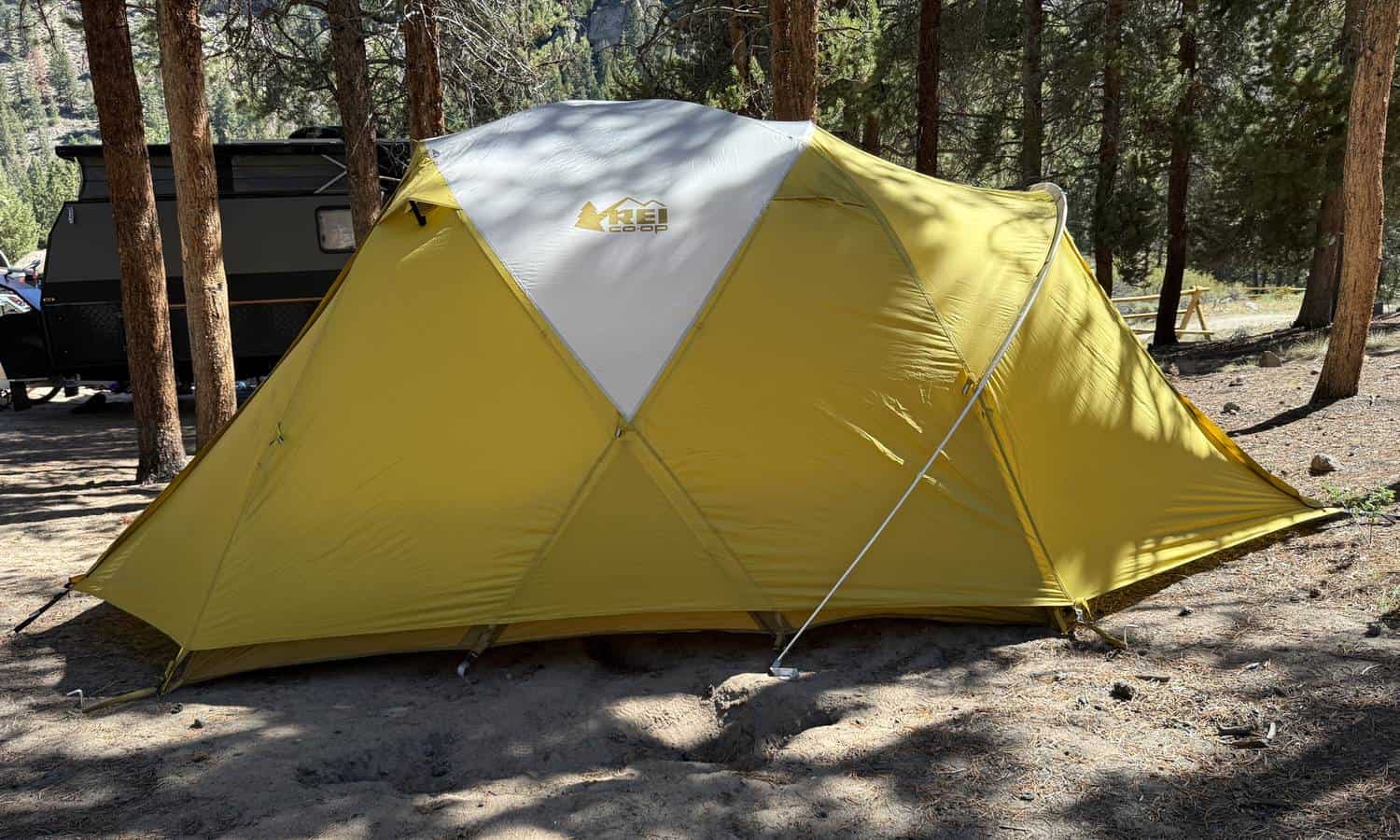 REI Co-op Base Camp 6 with its full yellow rainfly pitched at a pine forest campsite