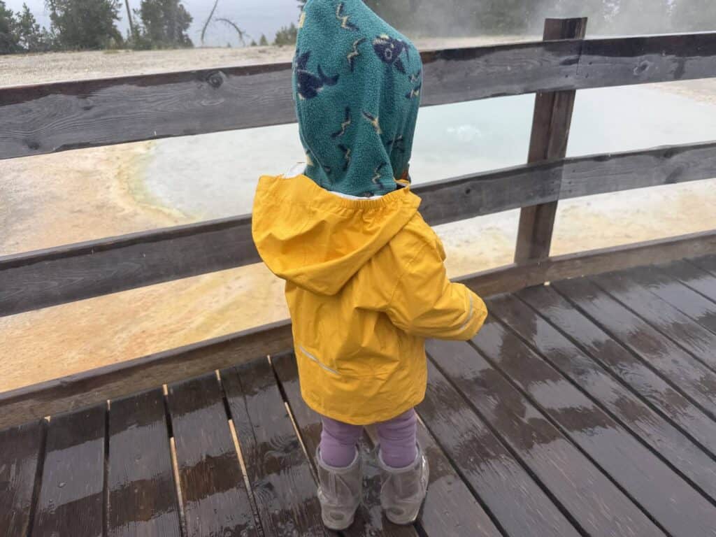 Toddler in yellow REI Co-op Rainier Rain Jacket standing at overlook above West Thumb geothermal pool at Yellowstone
