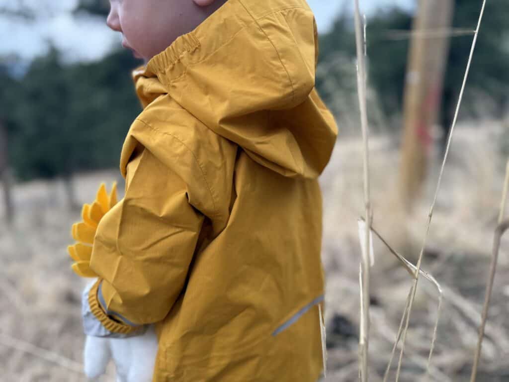 Close-up profile view of toddler wearing yellow REI Co-op Rainier Rain Jacket showing hood fit and soft fleece collar lining
