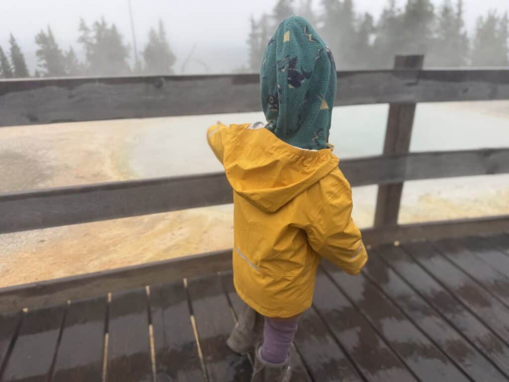 Toddler in yellow REI Co-op Rainier Rain Jacket pointing at geothermal pool at West Thumb Geyser Basin Yellowstone