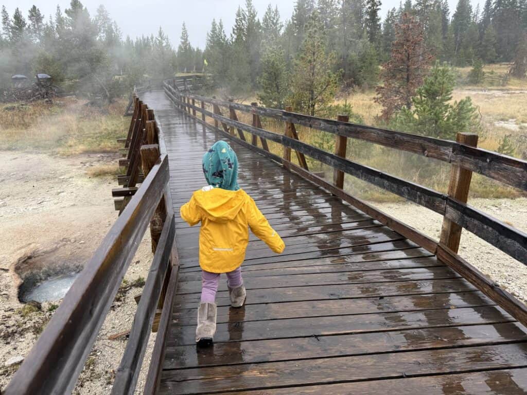 Toddler in yellow REI Co-op Rainier Rain Jacket running on wooden boardwalk at Yellowstone National Park