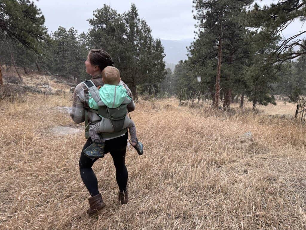 Toddler in yellow Reima Lampi Rain Jacket riding in a carrier backpack in snowy hiking conditions