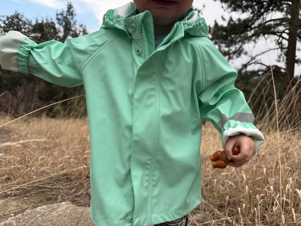 Toddler in yellow Reima Lampi Rain Jacket with arms spread showing front and reflective cuff strips