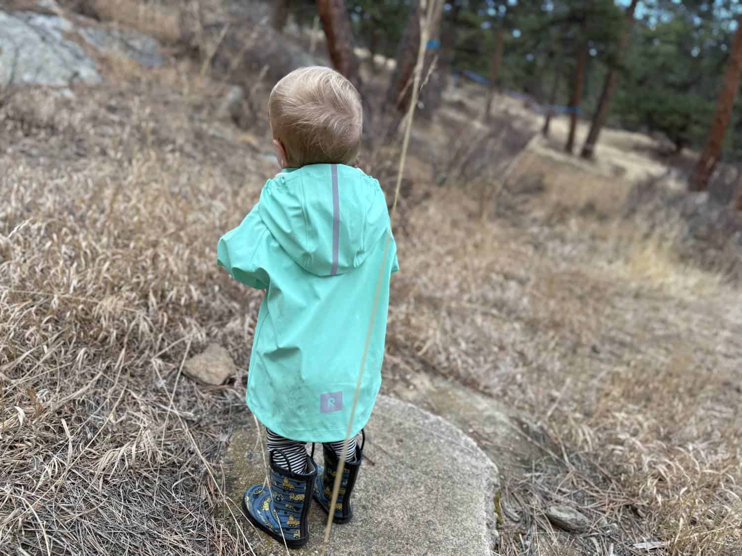 Full length back view of toddler wearing yellow Reima Lampi Rain Jacket on trail with Reima logo visible