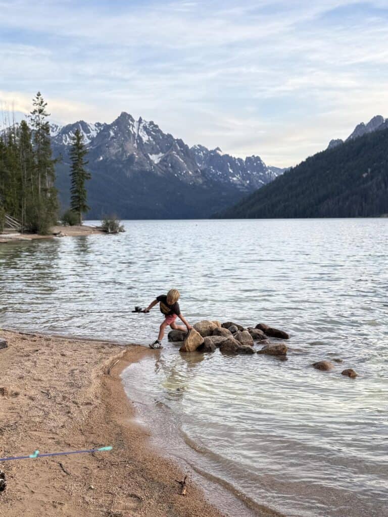 Kid climbing rocks at the edge of Redfish Lake, Idaho with the Sawtooth Mountains behind, wearing Salomon Speedcross shoes