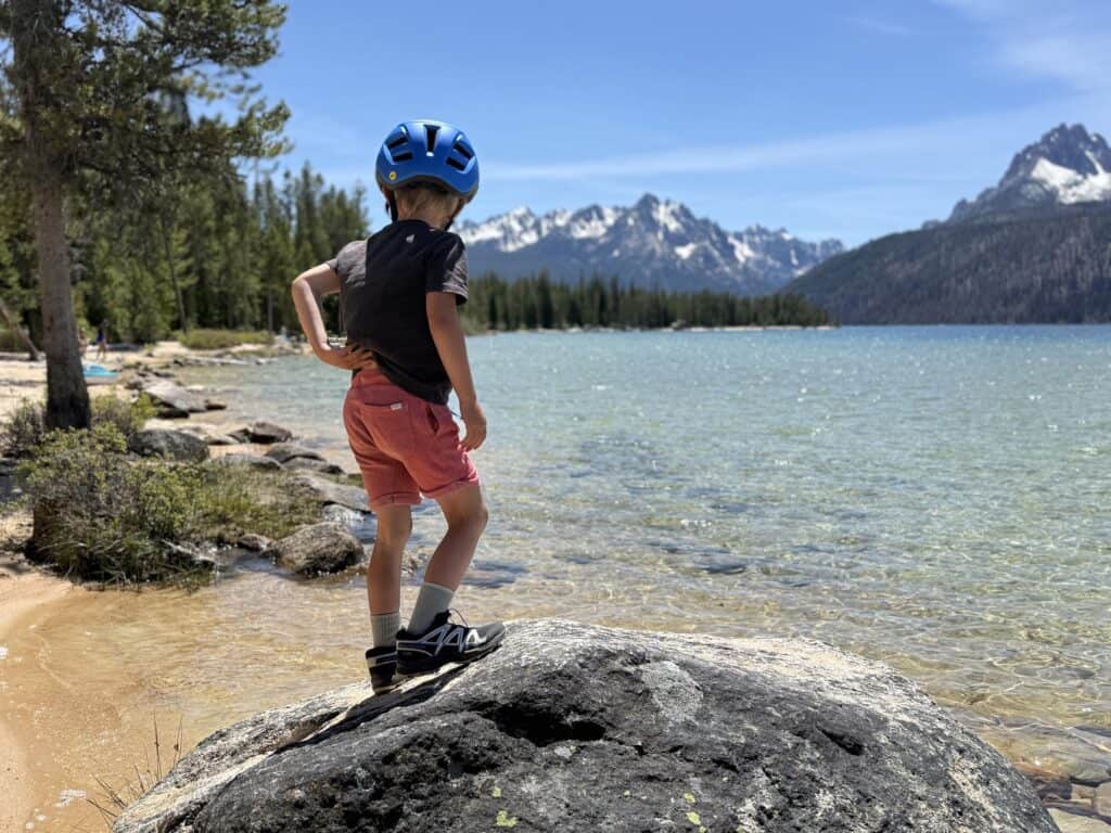Kid in a bike helmet standing on a boulder at Redfish Lake, Idaho wearing Salomon Speedcross shoes
