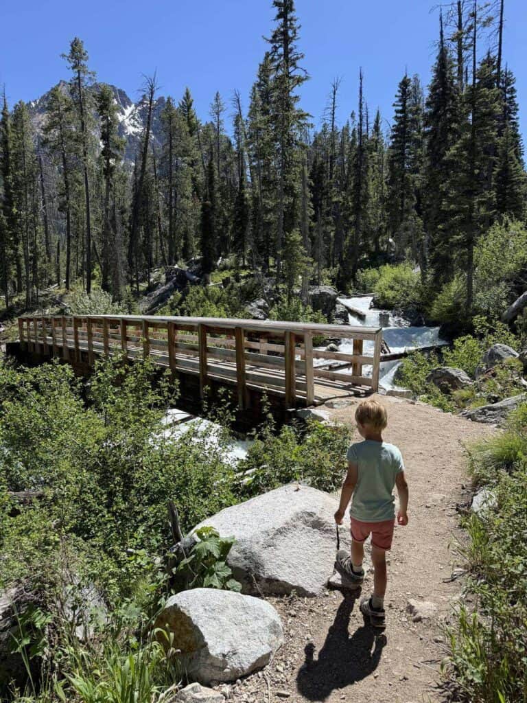 Kid hiking a trail toward a footbridge near Redfish Lake, Idaho in Salomon Speedcross shoes