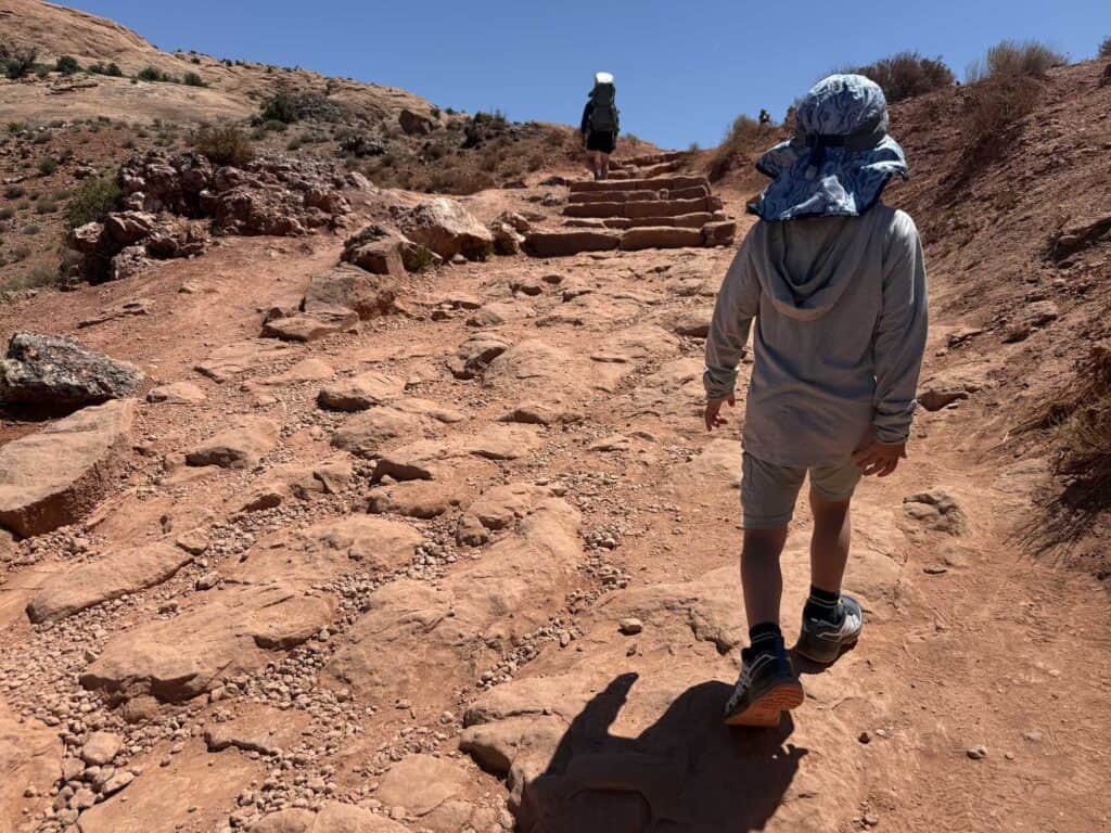 Kid in a sun hat hiking red rock steps on the Delicate Arch trail in Arches National Park in Salomon XA Pro V8 Waterproof shoes