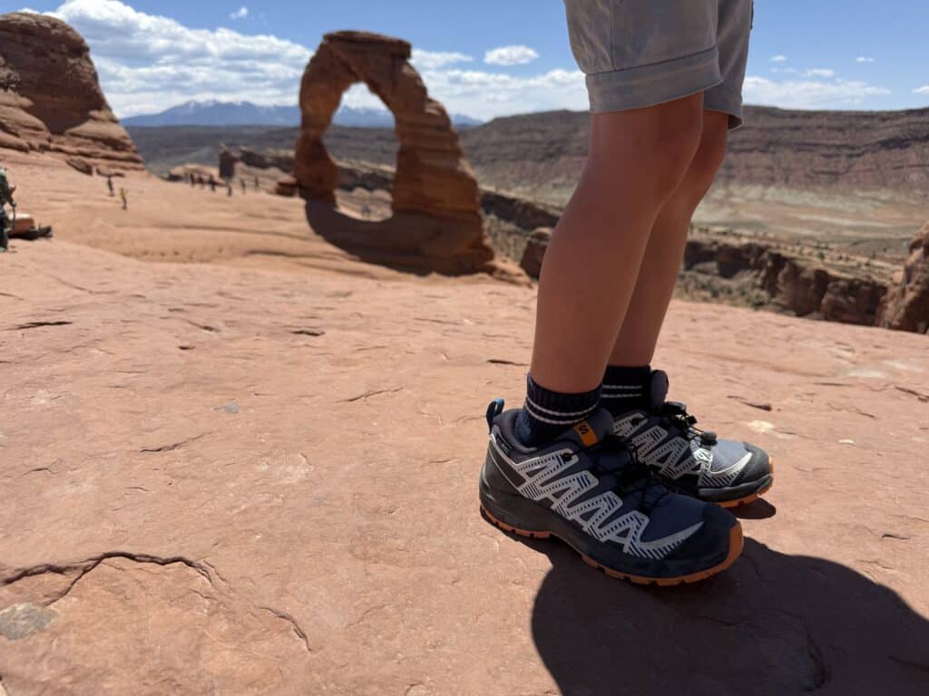 Salomon XA Pro V8 Waterproof kids shoes on slickrock with Delicate Arch in the background, Arches National Park, Utah