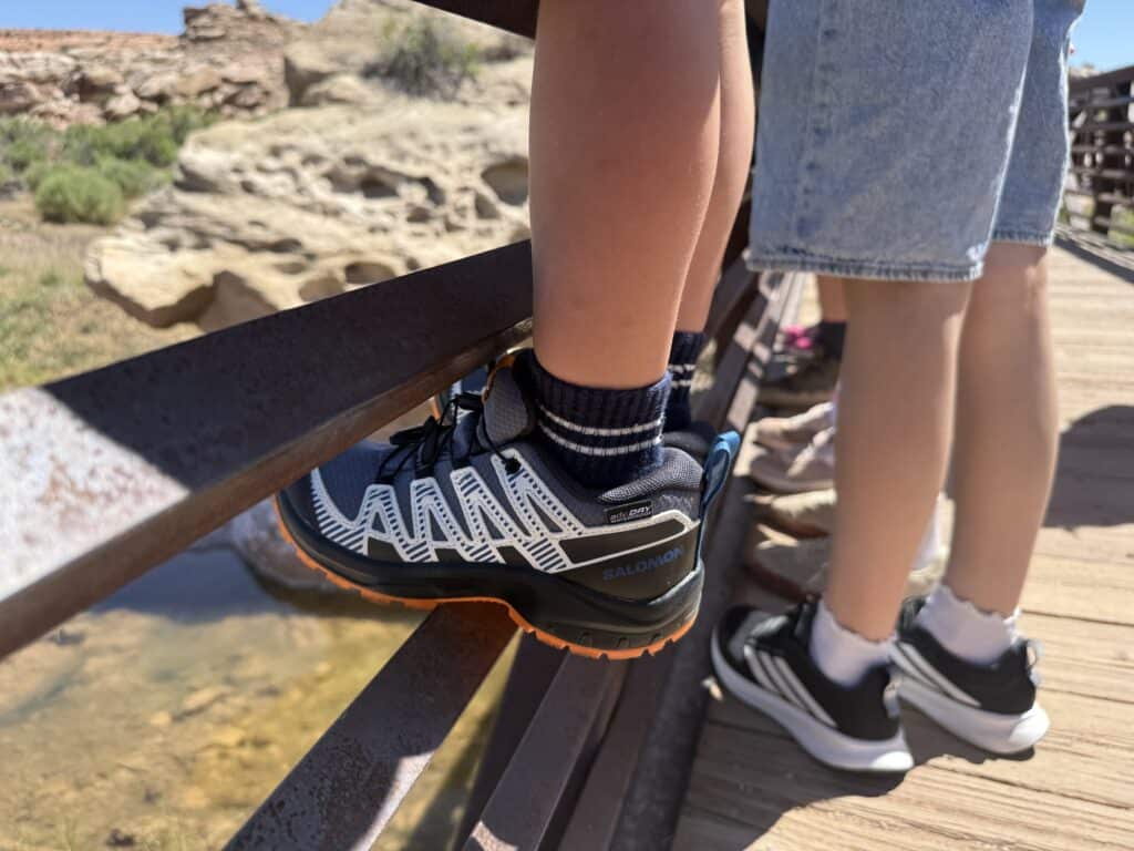 Salomon XA Pro V8 Waterproof kids shoe on a footbridge railing above a stream in Arches National Park
