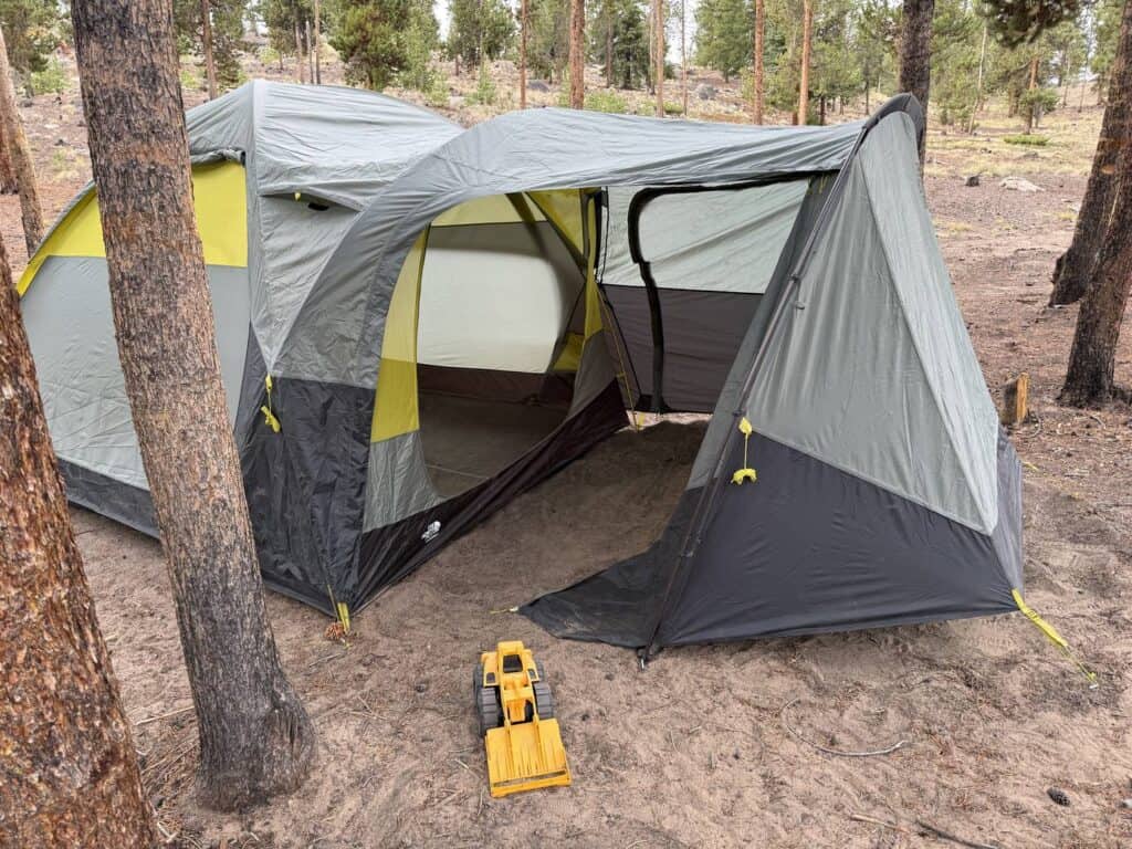 Yellow toy dump truck parked in front of The North Face Wawona 6 vestibule at a pine campsite